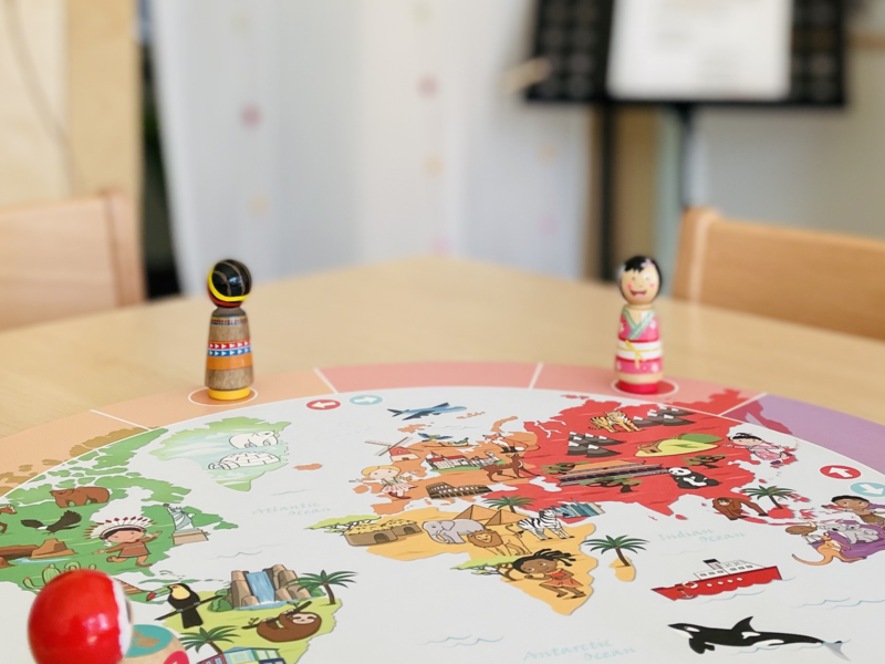 Aufgebautes Spiel auf einem Holztisch in einem Raum, im Hintergrund hängt an der Wan eine Gitarre und weitere Instrumente, es sind die Räumlichkeiten einer Kindertageseinrichtung